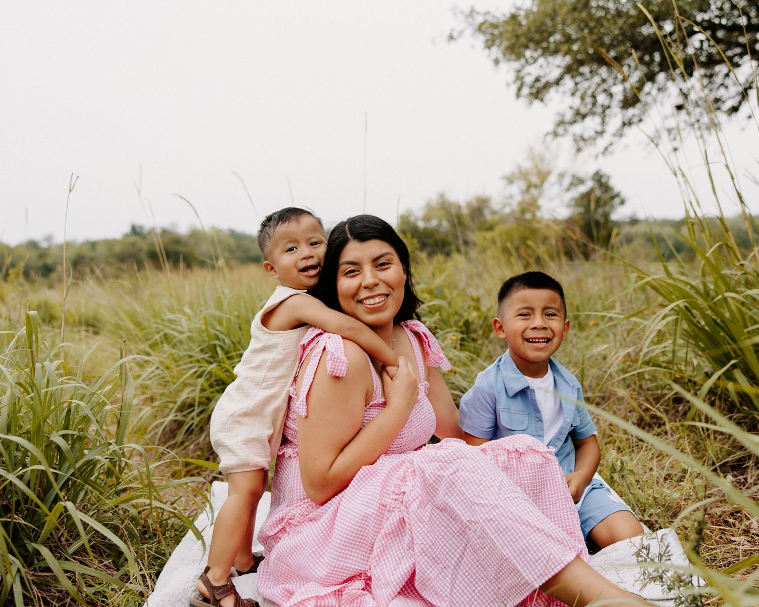 San Antonio Family Photography. Family sitting together in tall grass field wearing pink and blue casual attire.