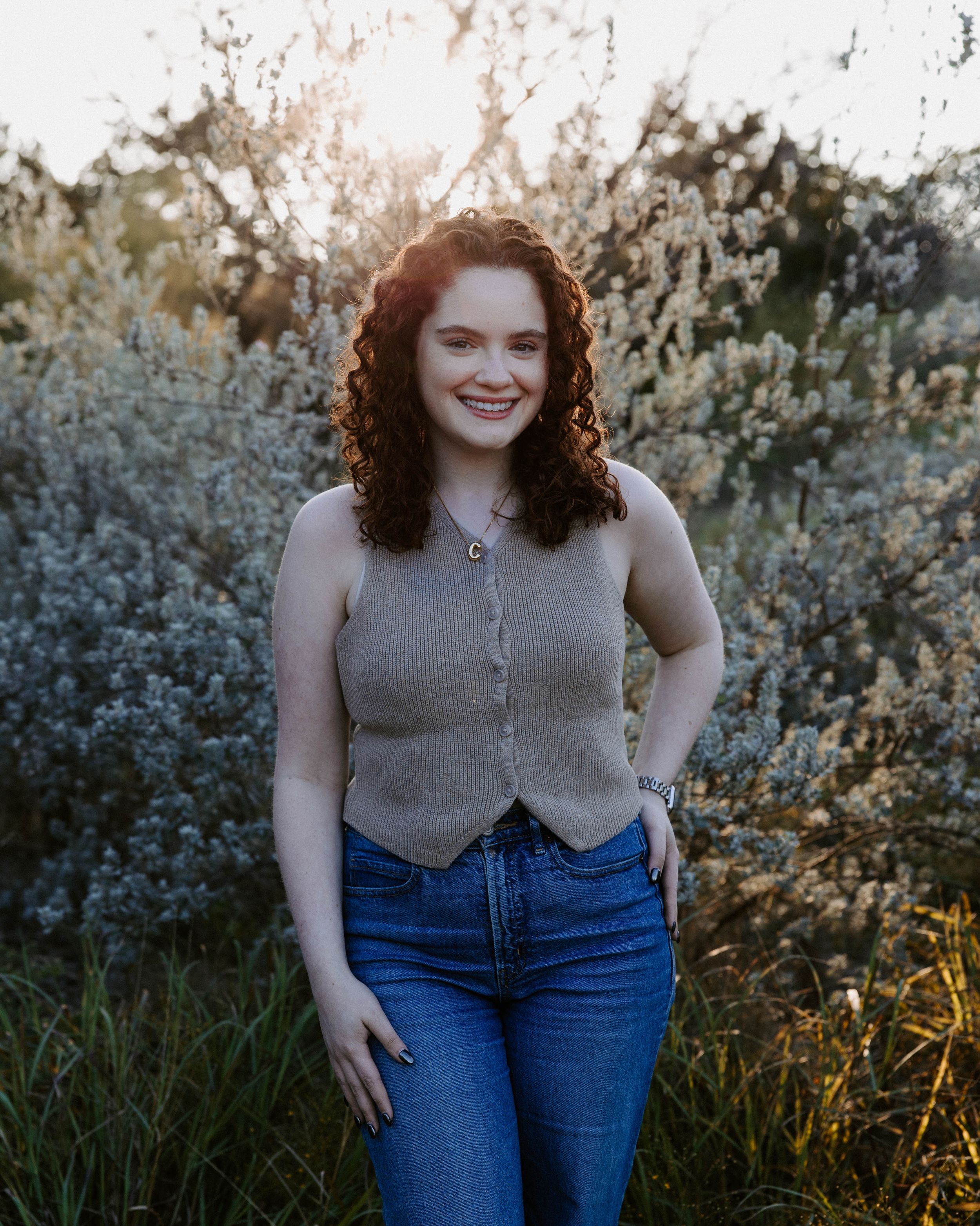 San Antonio Photographer Headshot. Person in knit tank top and jeans poses against flowering bushes in evening light.