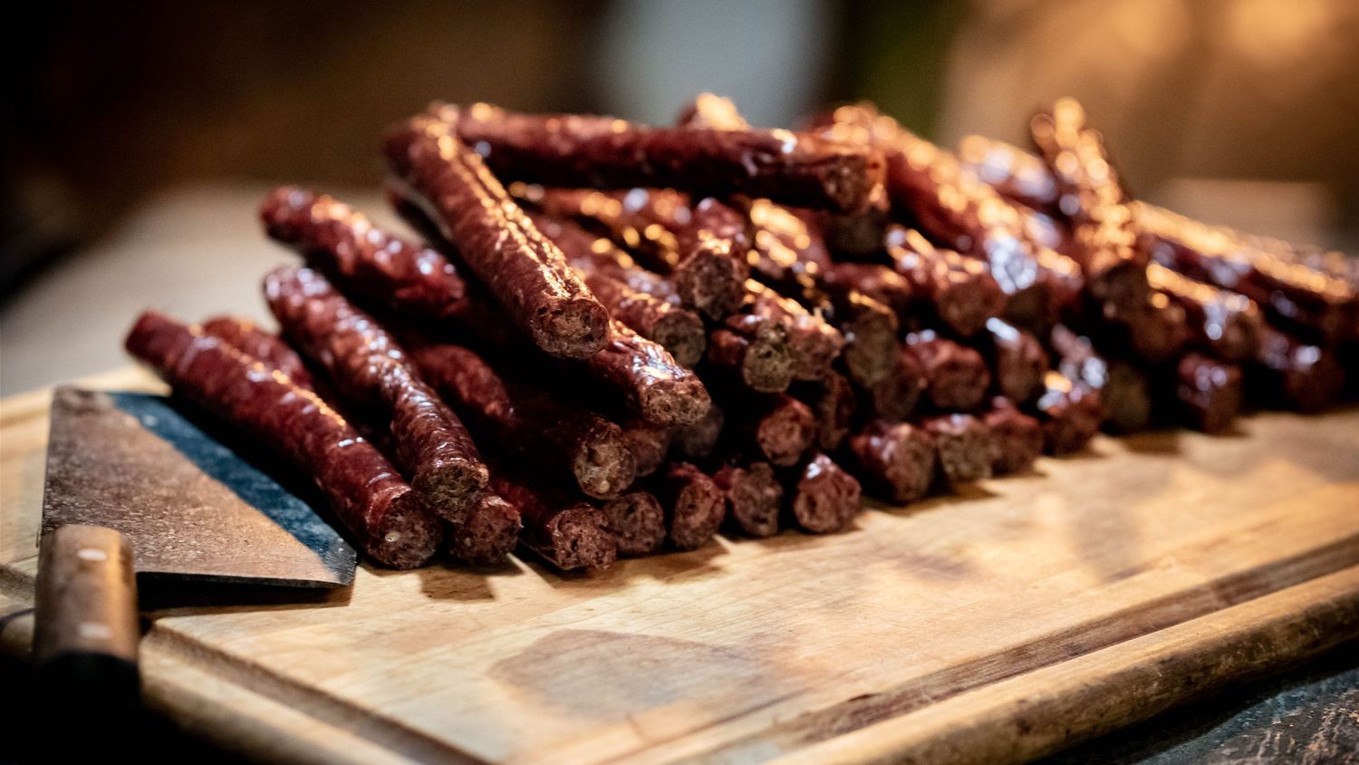 Smoked deer sausages arranged in neat rows on a wooden cutting board.
