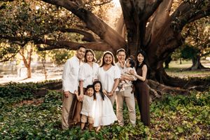 A group stands together under a large sprawling tree in a park during golden hour lighting.