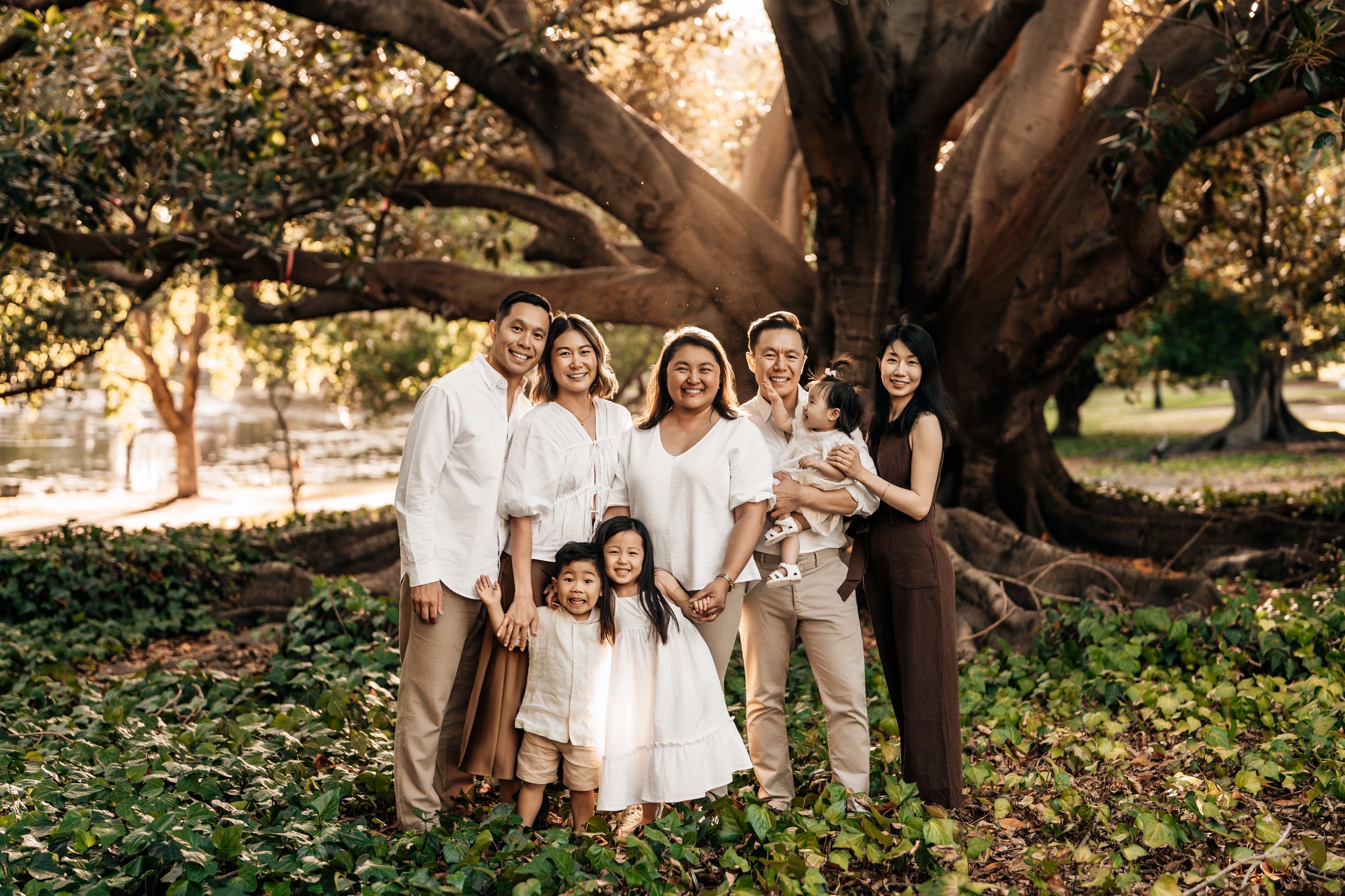 A group stands together under a large sprawling tree in a park during golden hour lighting.