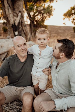 Three generations sit together on a fallen tree trunk at sunset.