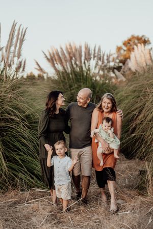 A joyful family walks together in tall ornamental grass during a warm sunset photoshoot.