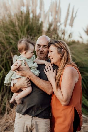 Three generations share a tender moment together outdoors among tall grass at sunset.