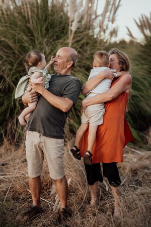 Two adults holding children pose together in front of tall grass during golden hour.