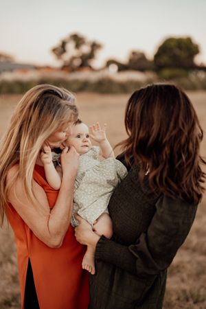 Two people share a special moment with a baby during sunset outdoors.