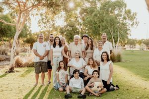 Large multigenerational family group portrait outdoors on green grass with trees in warm golden sunlight.