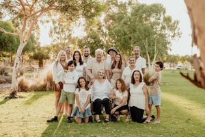 Large multigenerational family group smiling together outdoors in a sunny park with eucalyptus trees in Australia.