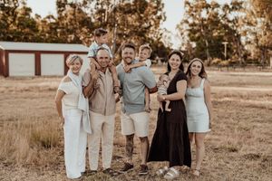 A group of people wearing coordinated neutral toned outfits pose together in a sunlit outdoor field at sunset.