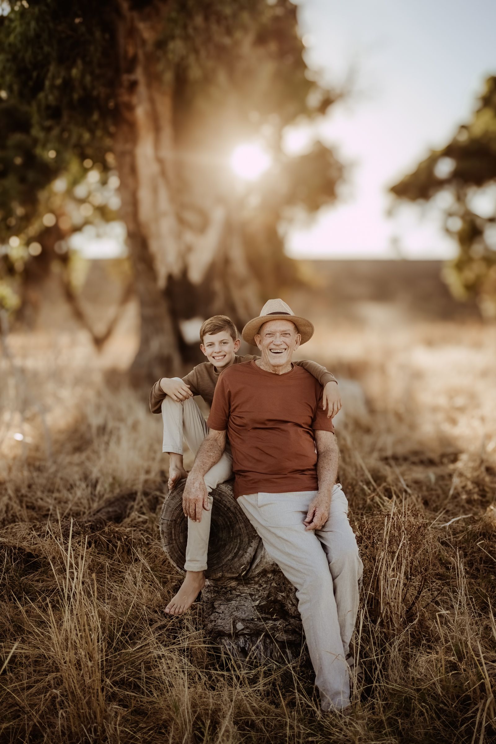 A sepia-toned portrait of two people sitting together on a hillside at sunset.