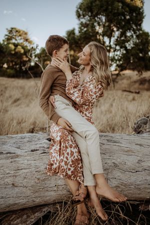 A romantic outdoor photoshoot featuring a couple sitting on a fallen log in warm sunlight.
