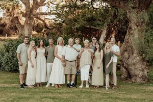 Large family group portrait outdoors on green lawn with large oak trees in warm golden light.