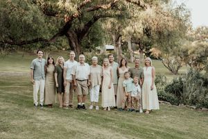 Large multigenerational family group portrait outdoors on green lawn beneath shady trees in warm natural light.