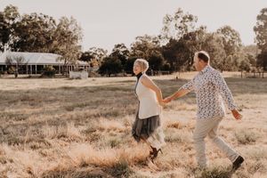 Joyful couple sharing a dance move in a grassy field with warm sunlight filtering through trees.