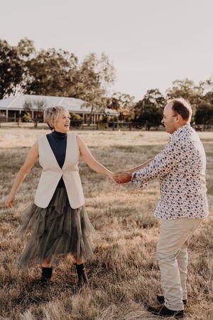 Dancing and twirling together in a field while wearing complementary outfits during sunset.