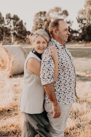 Couple embraces while posing in a rustic field setting with hay bales in the background.