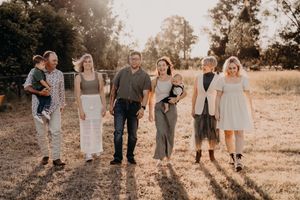 Family group poses together at sunset in casual attire on grassy field.