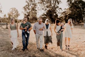 Extended family walking together through golden field at sunset in coordinated outfits.