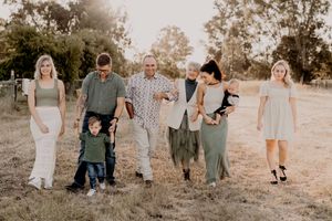 Multi-generational family group posed casually together in field during sunset.