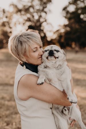 A heartwarming moment showing affection between a white fluffy dog and someone wearing a light-colored sleeveless top.
