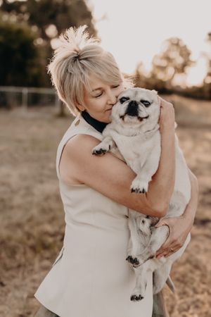 Sweet interaction between a person in white and their fluffy white dog in warm natural lighting.