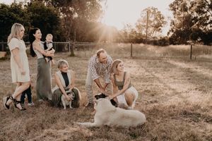 Family gathering in a grassy field during golden hour with pets and loved ones.