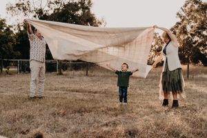 People holding a large white sheet outdoors during sunset in a grassy field.