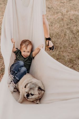 Child and dog lying together on a white sheet in warm natural lighting.
