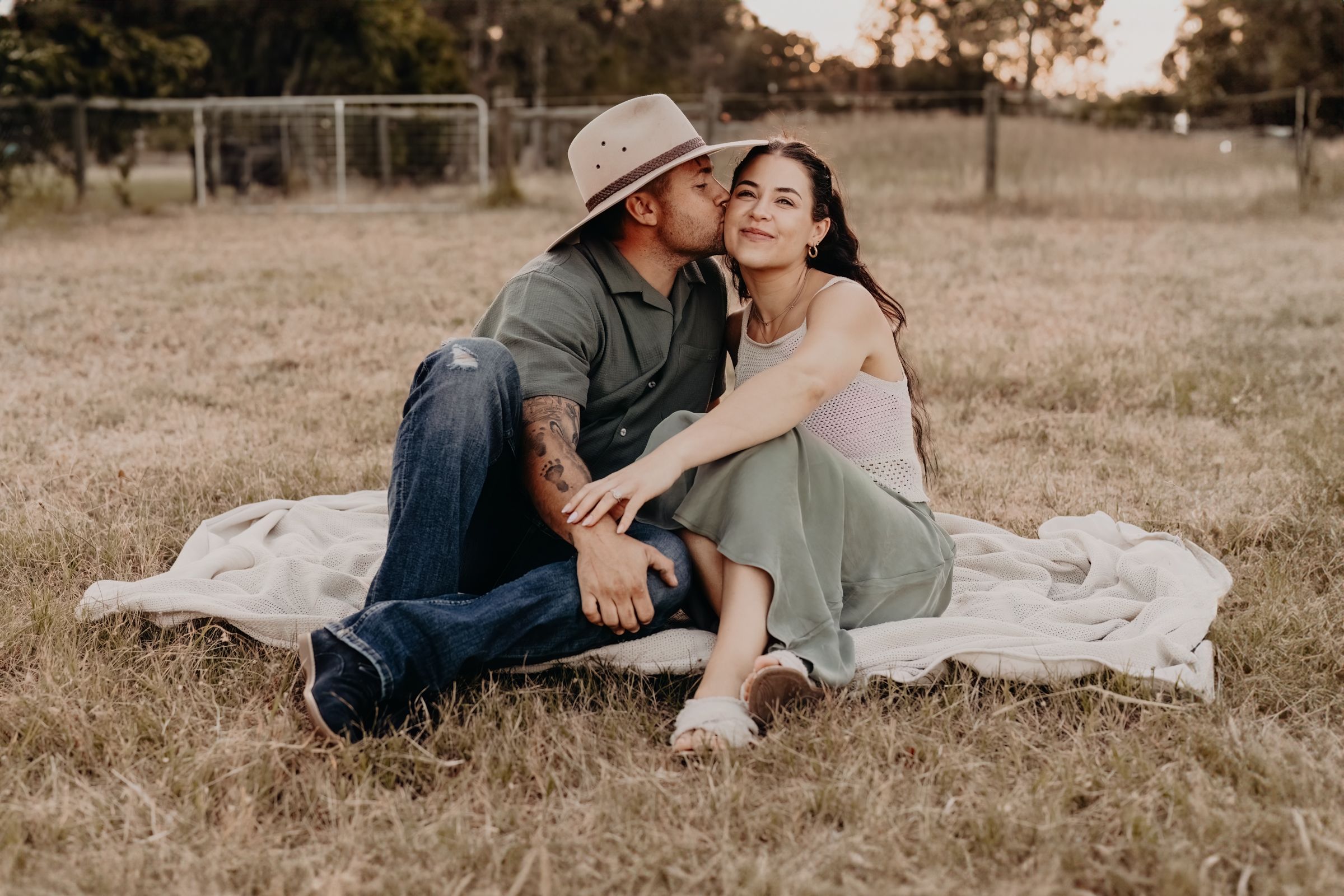 Playful couple photoshoot on white blanket in sunny field.