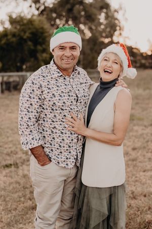 Festive couple wearing Christmas hats poses together outdoors.