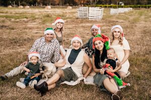 Family wearing holiday hats poses playfully on blanket during outdoor photo session.