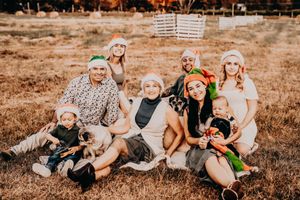 Family lounging together outdoors in a grassy field during sunset wearing festive holiday attire.