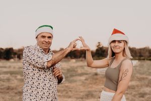 Two people in festive hats making heart shapes with their hands against a desert backdrop.