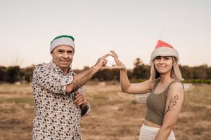 Two people in holiday hats forming a heart shape with their hands at sunset.