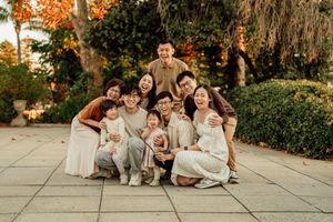 A joyful Asian family of nine poses together outdoors among autumn foliage for a warm group portrait.