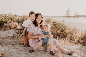 A small family group poses together on sandy ground with a pier visible in the background.