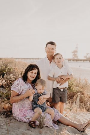 Family of four poses together on beach with distant pier visible in warm evening light.