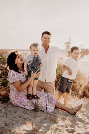 Family enjoying a casual moment together on sandy beach with pier in background.