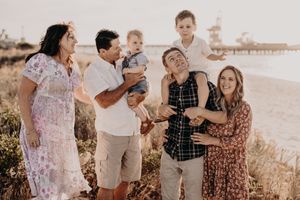 Extended family group laughing together during beach photoshoot at sunset.