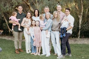 Extended family photo outdoors with grandparents, parents, and young children smiling together in a lush garden setting.