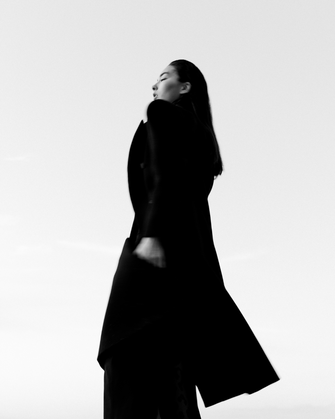 Dramatic black and white fashion portrait with figure in flowing black coat.