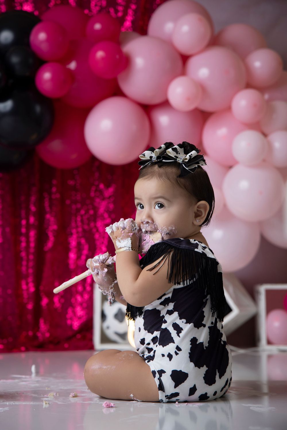 Festive cake smash photo session with pink balloons and sparkly backdrop.