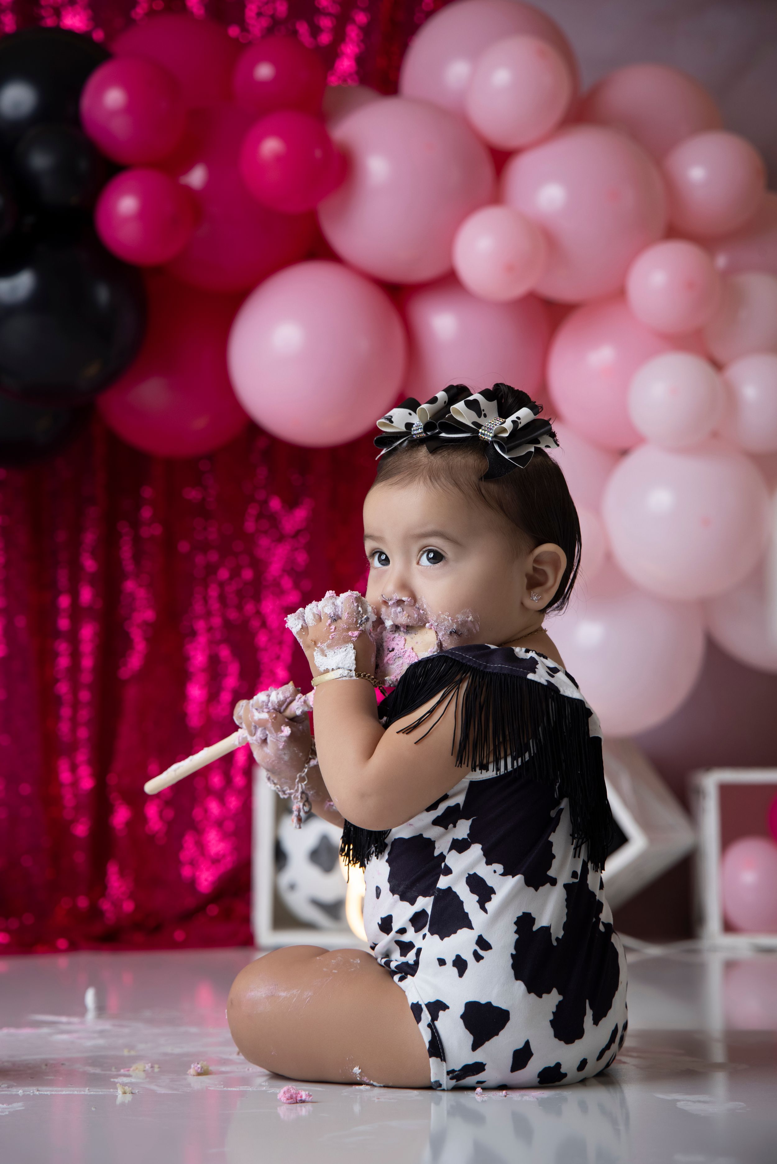 Festive cake smash photo session with pink balloons and sparkly backdrop.