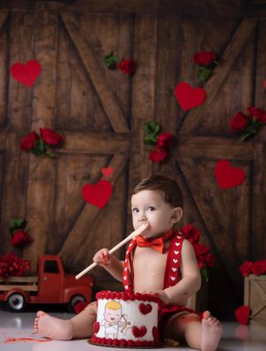Valentine's themed cake smash photo session with red hearts and rustic wooden background.