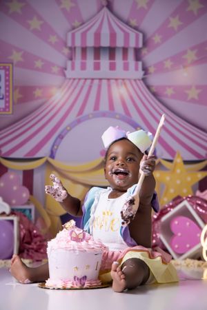 Cake smash photo session with circus-themed backdrop featuring pink and yellow stripes.