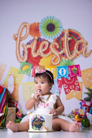 Colorful fiesta themed first birthday photo session with decorative paper fans and banners.