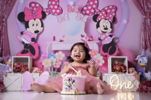 Pink Minnie Mouse themed first birthday cake smash photo session with decorative backdrop.