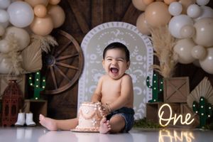 Rustic farmhouse cake smash setup with neutral balloon arch and wooden wheel backdrop.