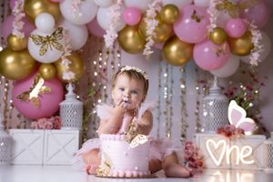 Elegant pink and gold balloon arch cake smash setup with sparkly decorations.