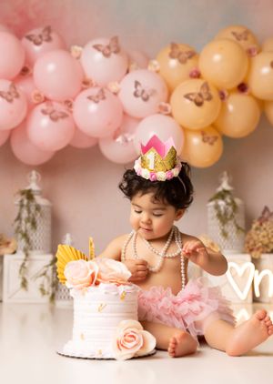 Pink and peach balloon garland backdrop for first birthday cake smash photography session.